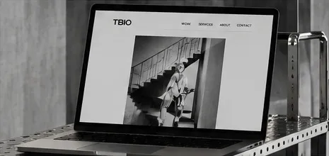 A laptop on a steel shelf showing a black-and-white TBIO website.
